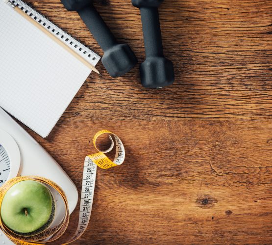 Fitness and weight loss concept, dumbbells, white scale, tape measure and notebook on a wooden table, top view